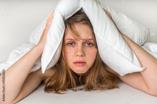 Woman in bed covering ears with pillow because of noise photo