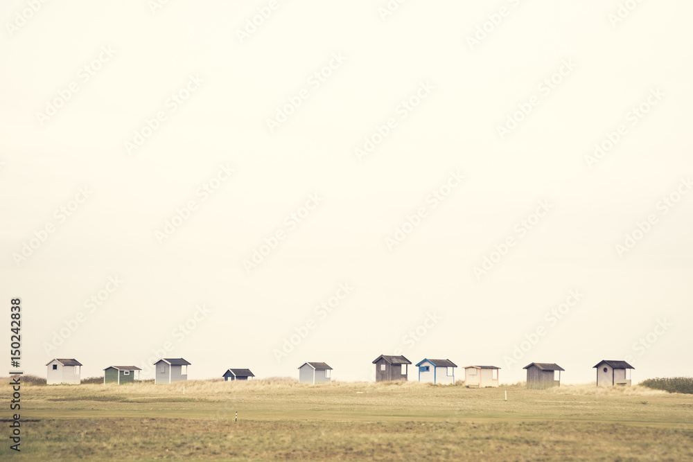 Obraz premium Small cute beach huts in a row at the shoreline on the horizon