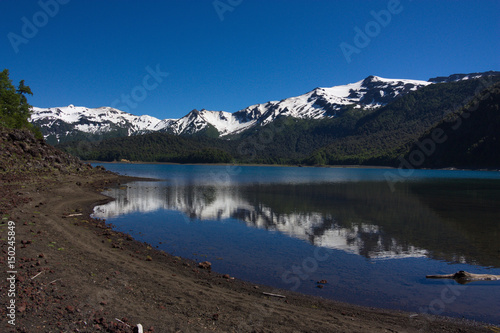 the black beach of the lake with the reflected mountains covered with snow in Conguillio National Park in Chile