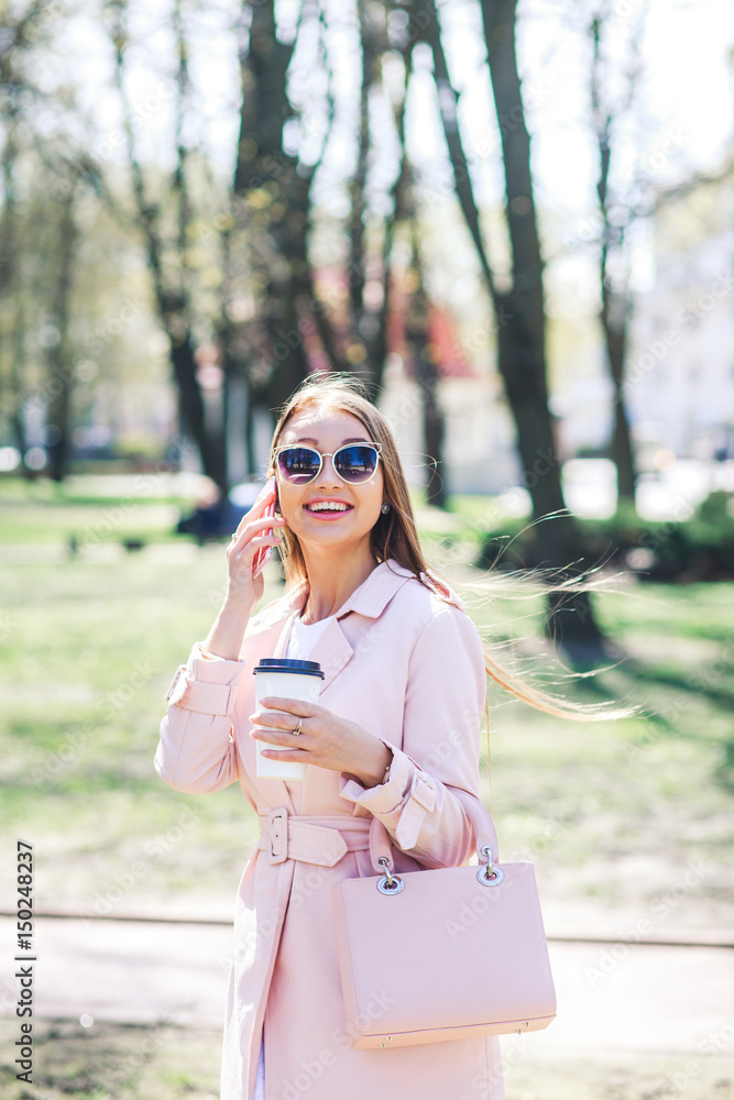 Fashionable woman with phone and cofee in the city. Fashion woman in a sunglasses and pink jacket outdoor