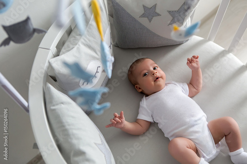 newborn lies in the round white bed with mobile and toys photo