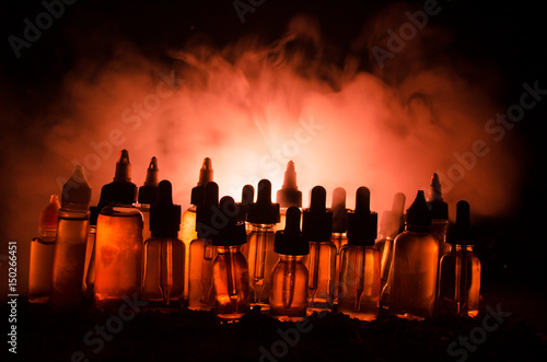 Vape concept. Smoke clouds and vape liquid bottles on dark background. Light effects.