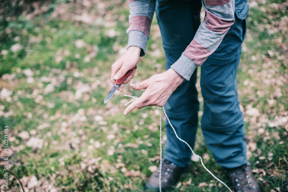 Hands of man cutting rope for preparing campsite. Hands of man cutting rope for preparing campsite.