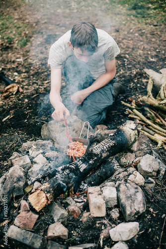 Wayfarer stirring meal in frying pan on campfire.