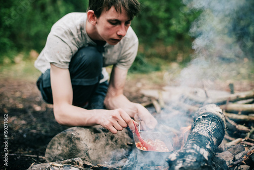 Wayfarer stirring meal in frying pan on campfire.