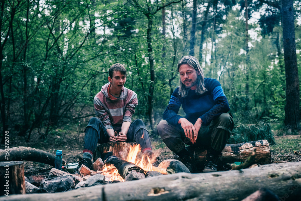 Obraz premium Two men sitting around campfire in spring forest.