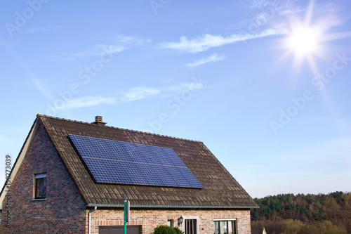 Photovoltaic panels on the roof of a residential building for alternative energy production in front of blue sky with sunshine and copyspace
