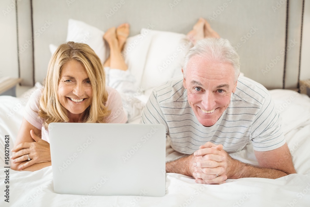 Portrait of smiling couple lying on bed and using laptop 