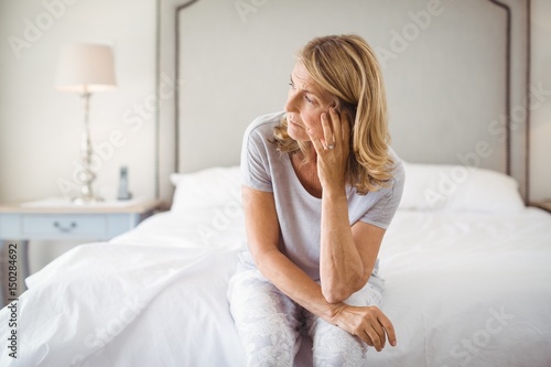 Tensed woman sitting on bed in bedroom