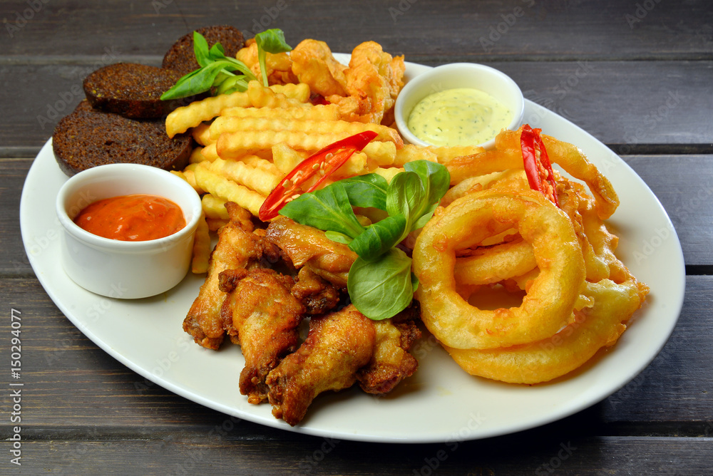 fried snacks Onion rings, chicken wings, bread with sauce on wooden table fried snacks Onion rings, chicken wings, bread with sauce on wooden table