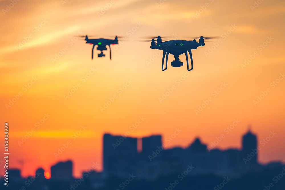 Two modern Remote Control Air Drones Fly with action cameras in dramatic sunset sky. Cityscape silhouette in the background. Modern technologies. Close up. Kiev, Ukraine. Travel, hobby, inspiration