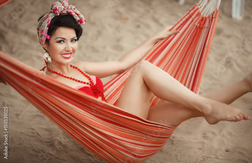 Beautiful pinap woman smiling in red bikini outdoor at beach. Pin-up girl retro style model in California coast. Tropical beauty lady at summer vacation.