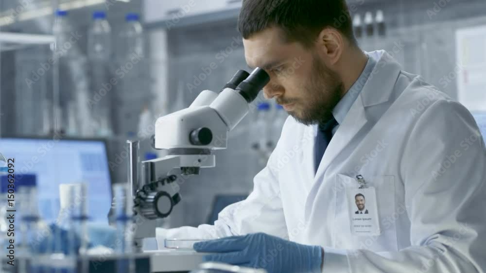 In a Modern Laboratory Assistant Brings Petri Dish to Chief Research Scientist who Starts Examining given Sample Under Microscope. Shot on RED EPIC-W 8K Helium Cinema Camera. In a Modern Laboratory Assistant Brings Petri Dish to Chief Research Scientist who Starts Examining given Sample Under Microscope. Shot on RED EPIC-W 8K Helium Cinema Camera.