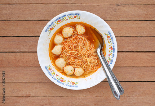 Top view instant noodles with meat balls in ceramic bowl against wooden plank.