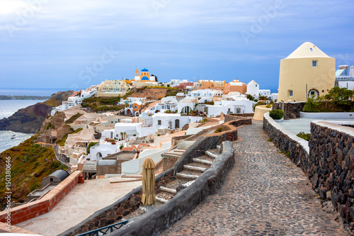 Oia town on Santorini island, Greece. Traditional and famous houses and churches with blue domes over the Caldera, Aegean sea, clouds.