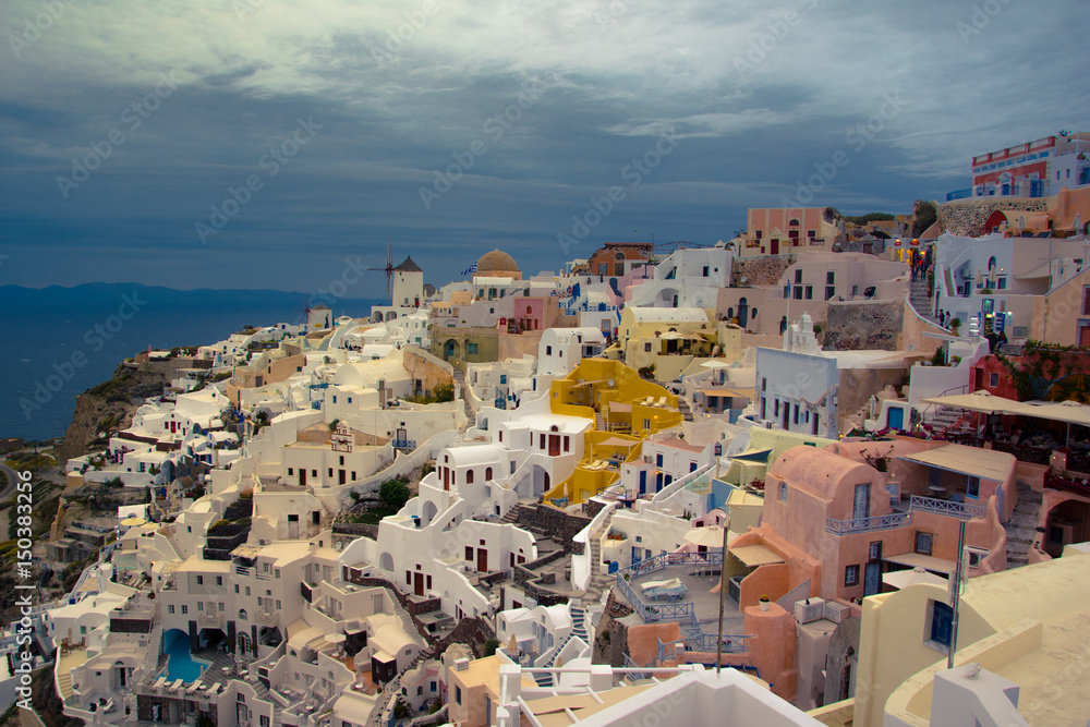 Oia town on Santorini island, Greece. Traditional and famous houses and churches with blue domes over the Caldera, Aegean sea, clouds.