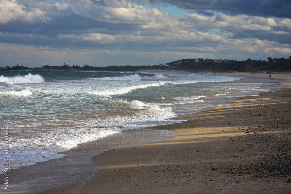 Sandy beach with long white surf waves in Coffs Harbour in late evening light.