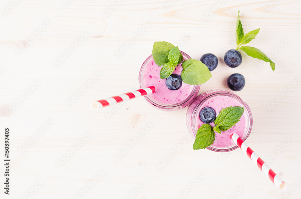 Freshly blended violet blueberry fruit smoothie in glass jars with straw, mint leaves, berries, top view. White wooden board background, copy space.