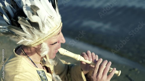 An Indian in a national costume plays a flute on the river bank 4k