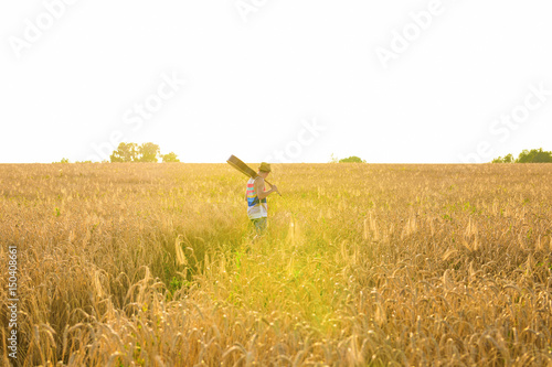 Musician holding acoustic guitar and walking in summer fields at sunset.