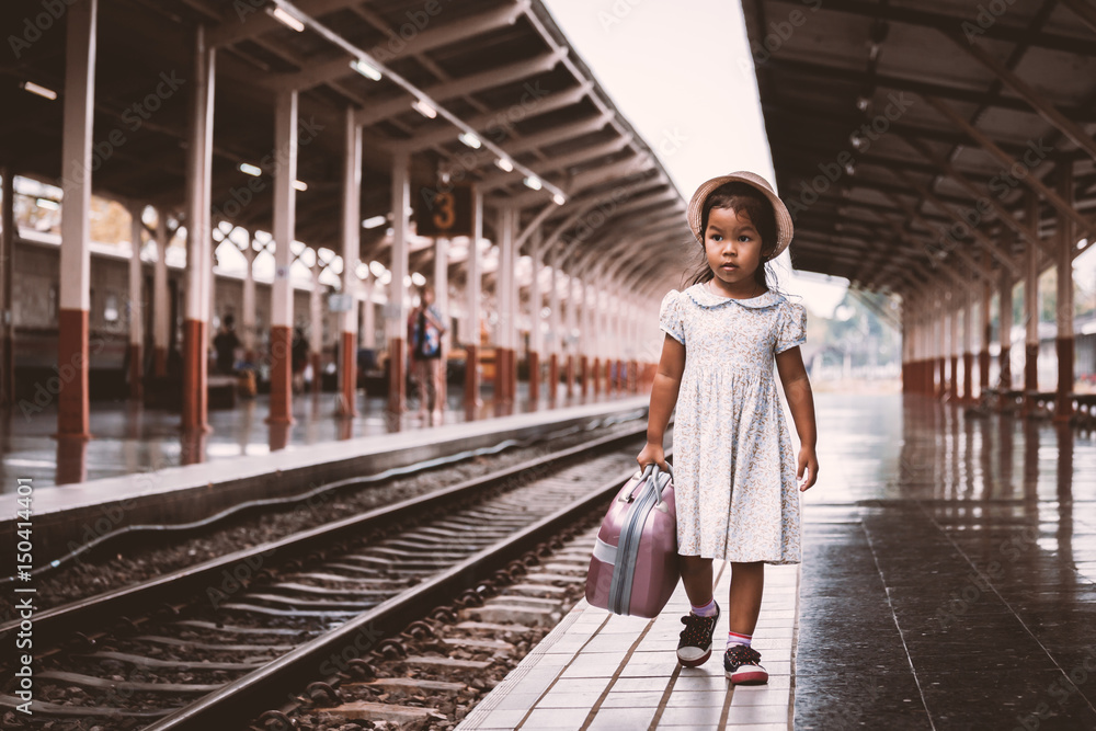 Cute asian little girl holding suitcase and walking on a railway station in vintage retro style