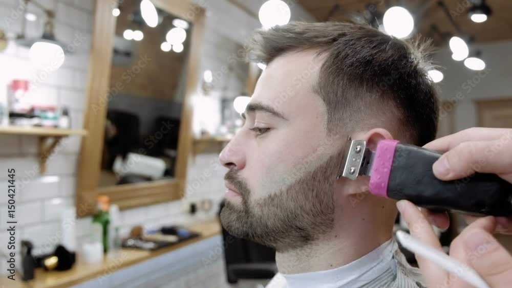 Master cuts hair and beard of men in the barbershop, hairdresser makes hairstyle for a young man Master cuts hair and beard of men in the barbershop, hairdresser makes hairstyle for a young man