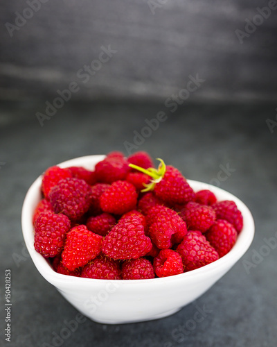 Fresh raspberries in heart shape bowl on dark background with space for text.