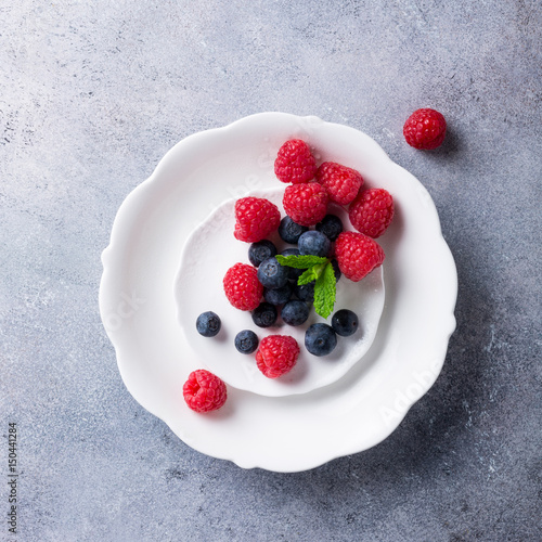 Freshly picked blueberries and raspberries on white plate on gray stone background. Concept for healthy eating and nutrition with copy space. Top view.