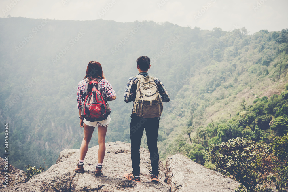 Hikers couple with backpacks standing on top of a mountain and enjoying nature view