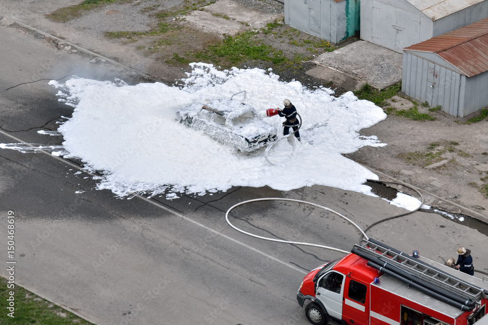 Obraz premium Firefighters are extinguished by a foam burning car. The work of special rescue services.