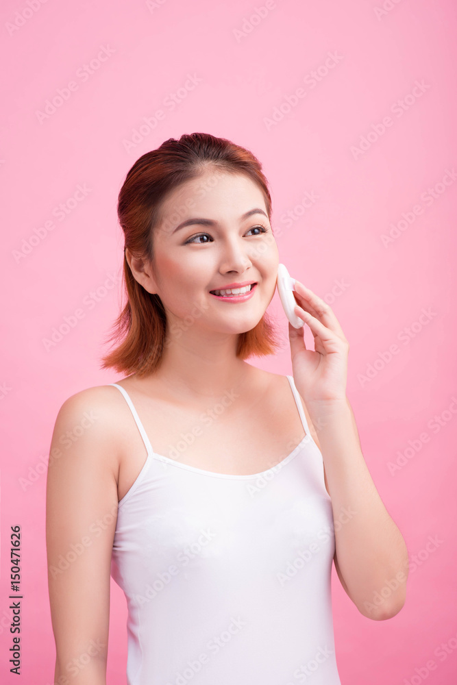 Young lady applying blusher on her face with powder puff, skin care concept on pink background. Young lady applying blusher on her face with powder puff, skin care concept on pink background.