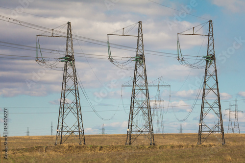 Electricity pylons and lines at summer field, sunny day photo