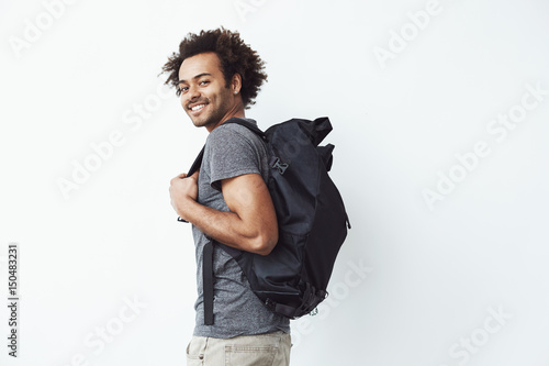 Cuadro en lienzo Handsome african man with backpack smiling standing against white wall ready to go hiking or a student on his way to university