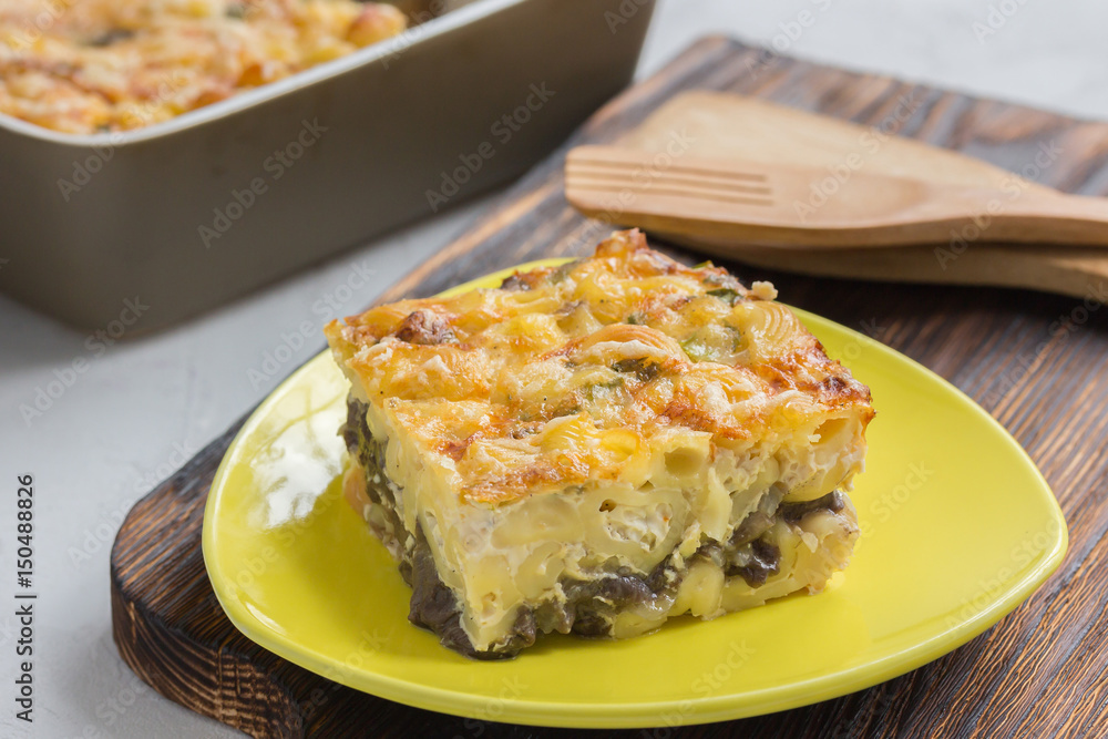 A piece of macaroni and cheese on a plate on wooden board. Baked pasta casserole in a ceramic baking dish. A piece of macaroni and cheese on a plate on wooden board. Baked pasta casserole in a ceramic baking dish.