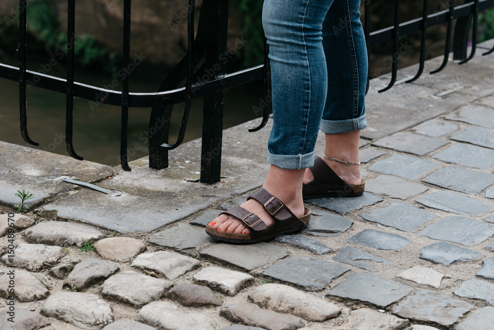 Young woman wearing sandals in cobblestone pavement of medieval city