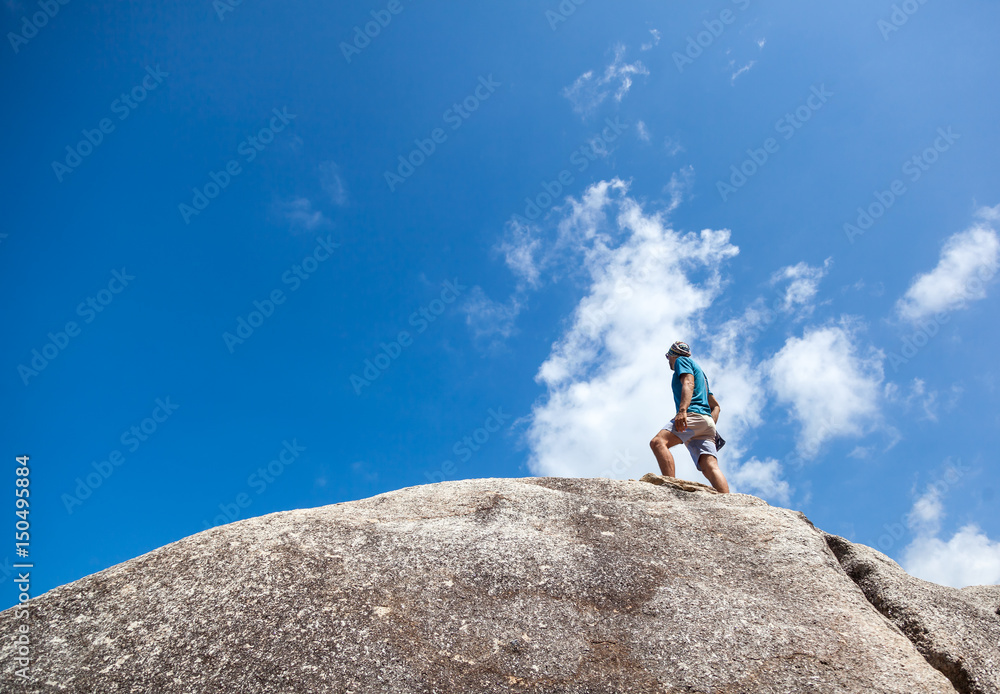 A man traveler stands on a mountain against a blue sky and clouds
