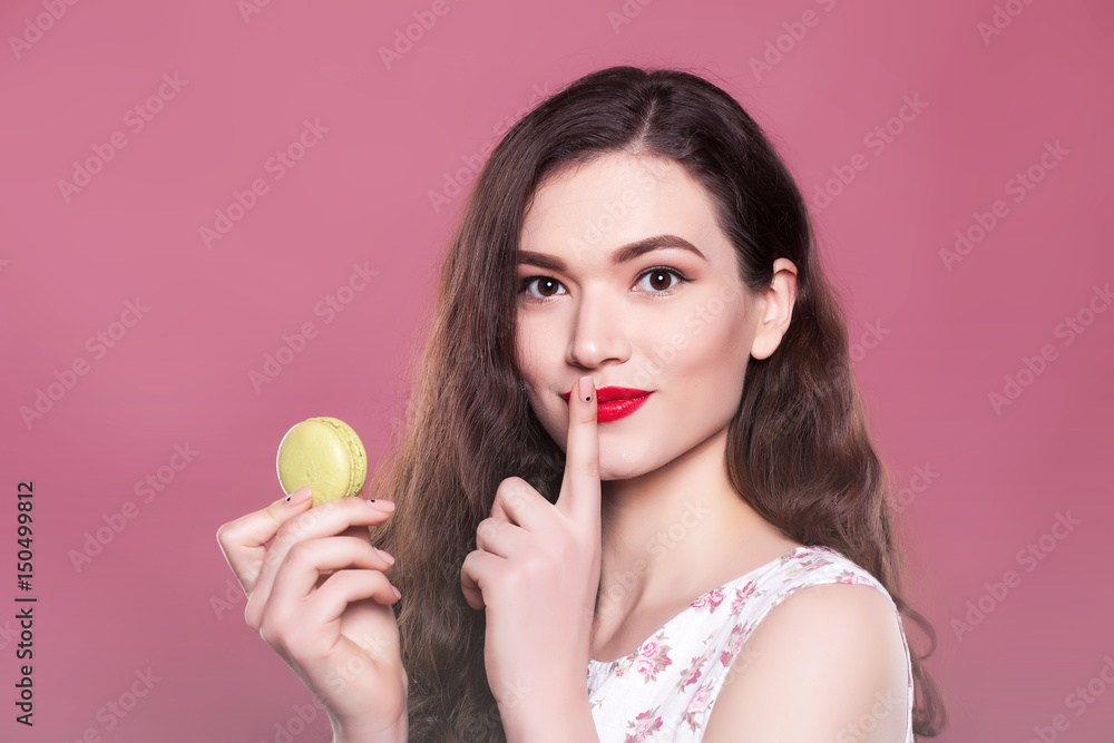 Beautiful girl holds a macaroon and shows signs on a pink background Beautiful girl holds a macaroon and shows signs on a pink background
