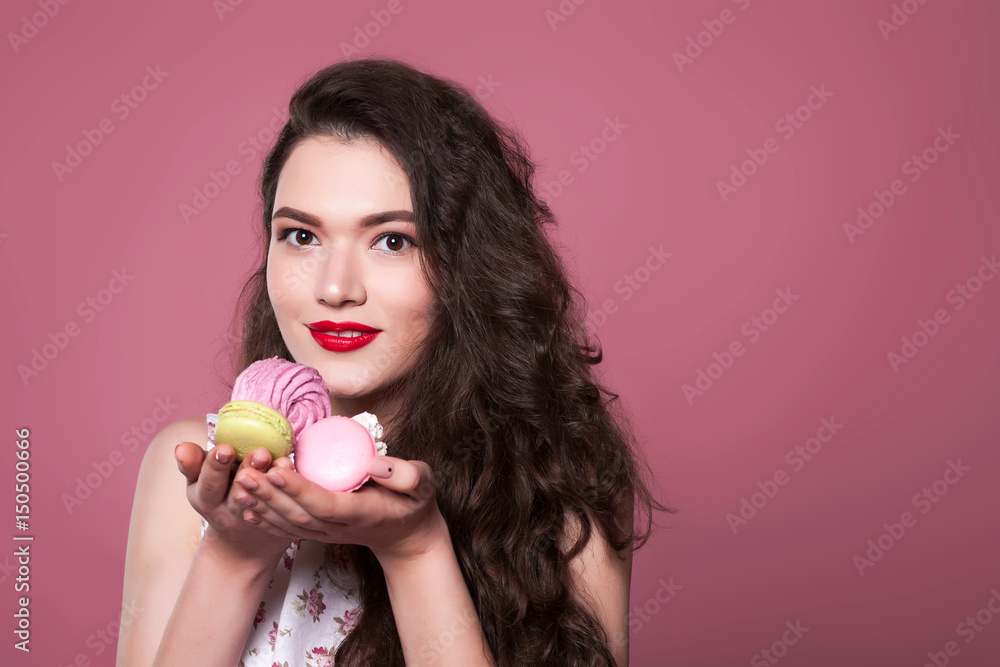 Beautiful young girl holds Macaroons and marshmallows on a pink background Beautiful young girl holds Macaroons and marshmallows on a pink background