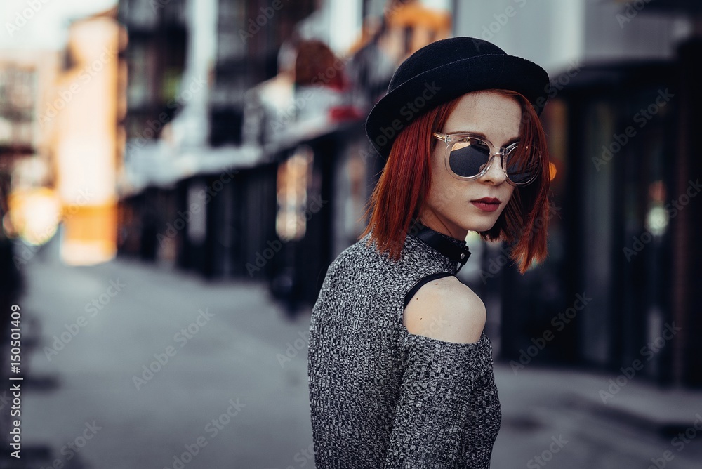 Outdoor portrait of young beautiful fashionable lady walking on the old street. Model wearing wide-brimmed hat and stylish clothes. Girl looking down. Female fashion concept. City lifestyle.