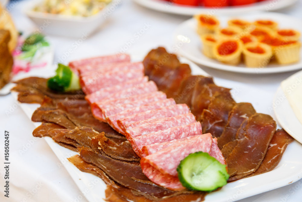 Slices of different sausages and meat lying on a plate on a festive table