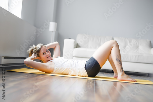 Full length portrait of attractive young woman working out at home in living room, doing yoga or pilates exercise