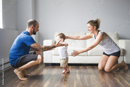 Cheerful mom and dad help their son to walk at home