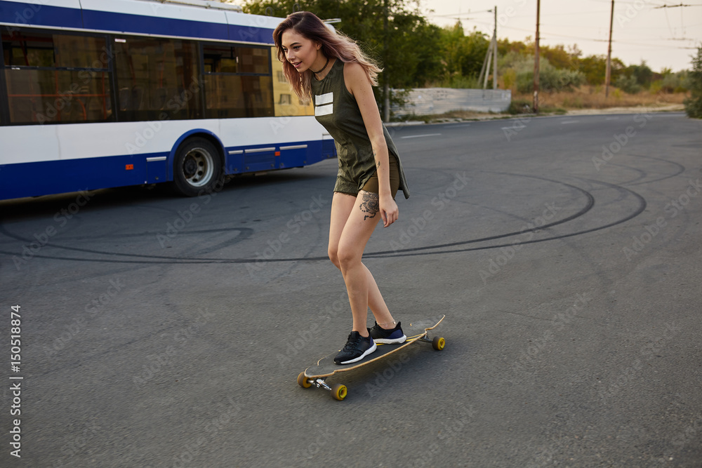 Beautiful young girl with tattoos riding on his longboard on the road in the city in sunny weather. Extreme sports Beautiful young girl with tattoos riding on his longboard on the road in the city in sunny weather. Extreme sports