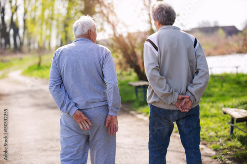 View from behind of an adult son walking with his senior father in the park.