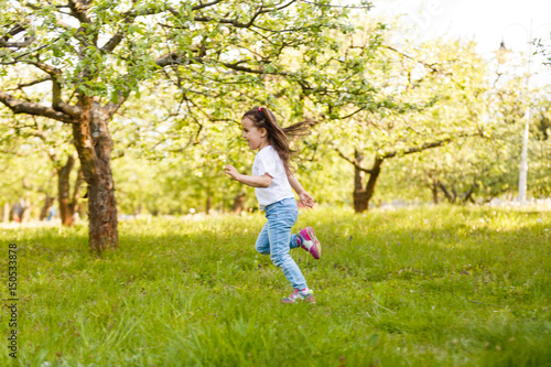 little girl blows off fluff from a bouquet of dandelions, standing in the middle of an apple orchard