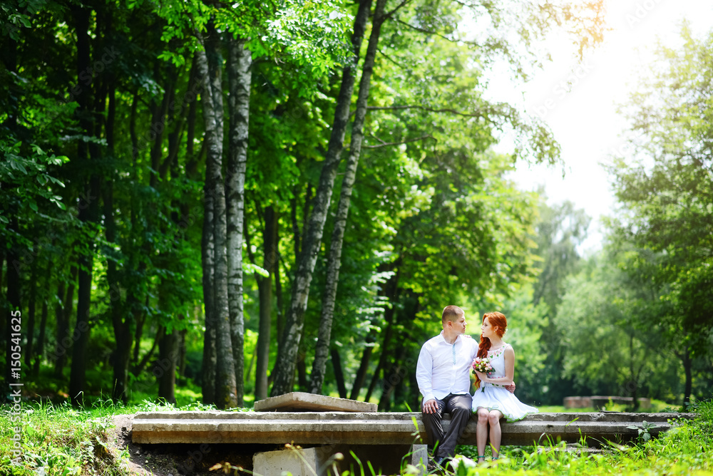 Fototapeta premium Groom fixes his blue bow tie standing before the bride on old stone bridge