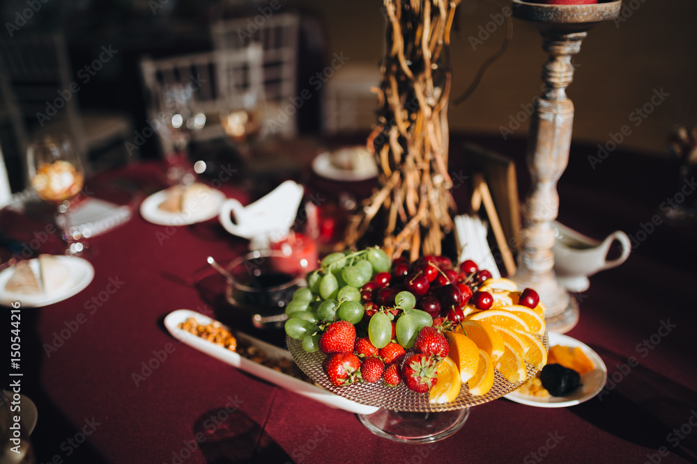 On the festive table in the wedding banquet area there are candles, plates, glasses and a dish with fruits and berries