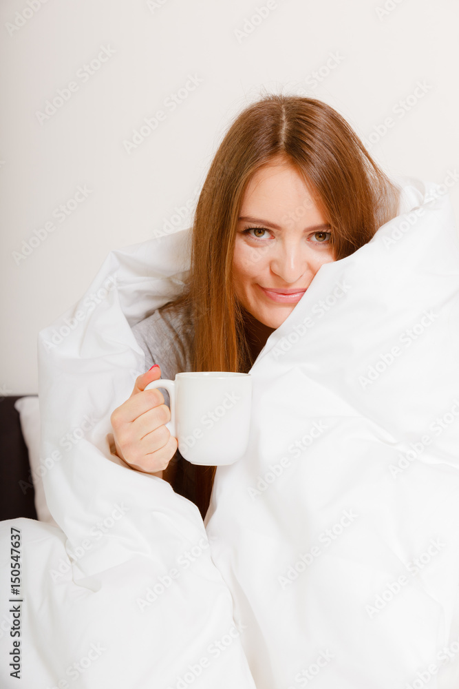 Smiling woman holding cup of drink in bed Smiling woman holding cup of drink in bed
