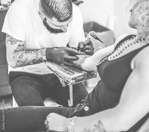 Professional bearded tattoo artist making tattoo in his own ink studio on young blond woman photo