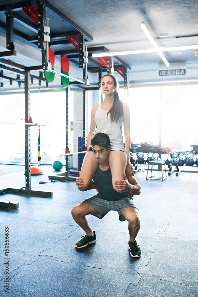Obraz premium Man carrying woman on his shoulders, doing squats.